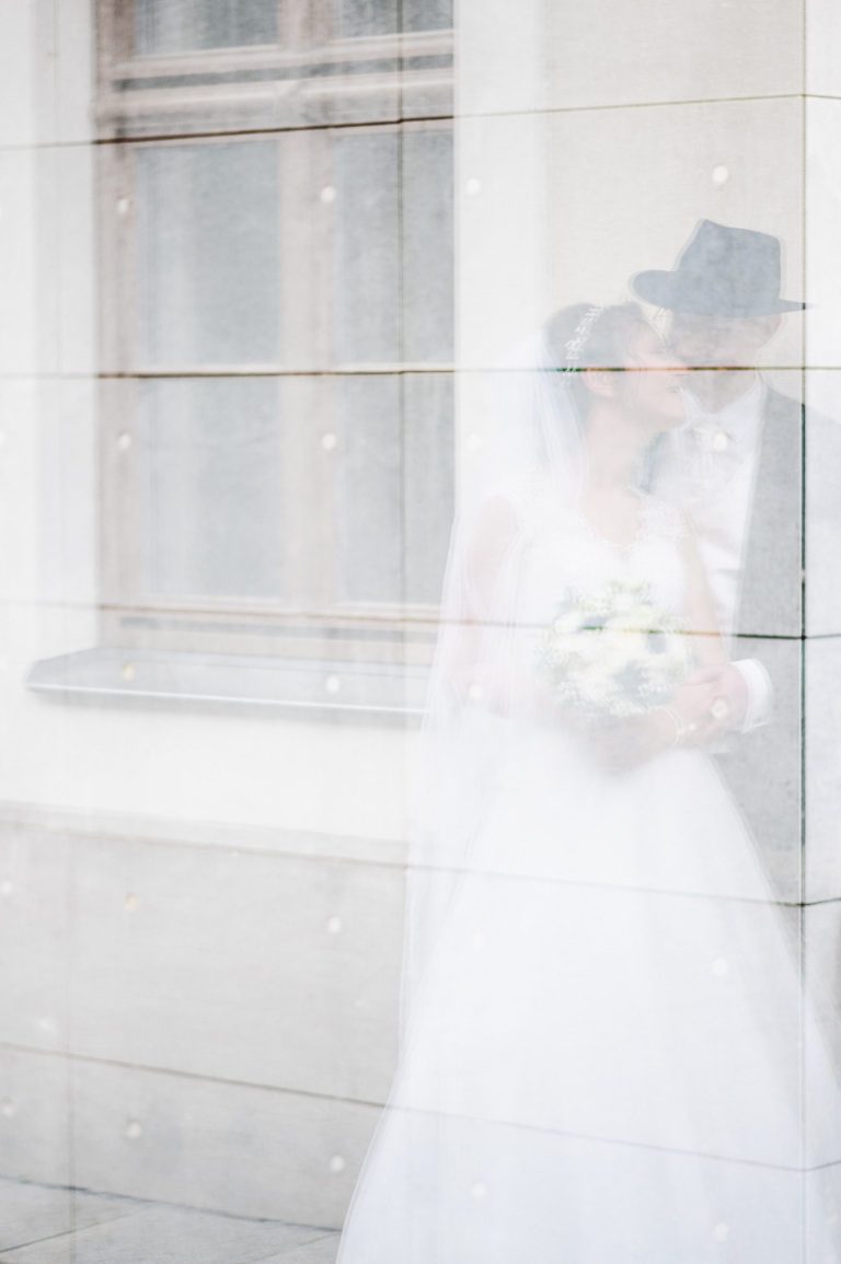 Braut und Bräutigam in Hochzeitskleidung umgeben von einem zarten Schleier.