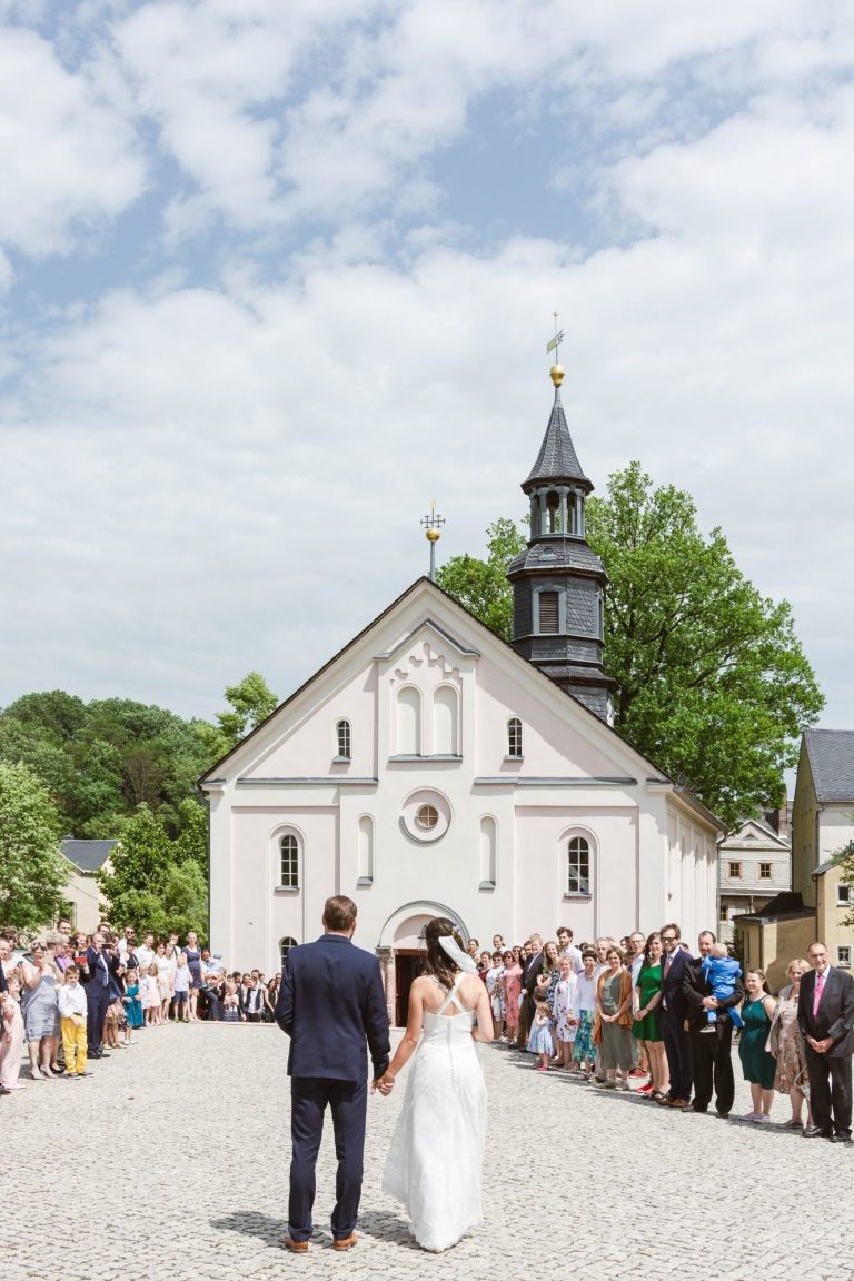 Brautpaar steht vor einer Kirche, umgeben von Gästen bei einer Hochzeitszeremonie.